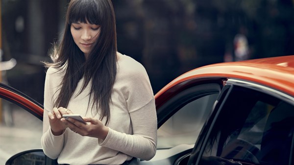 Woman using her mobile seamlessly near her Renault car with the front door open