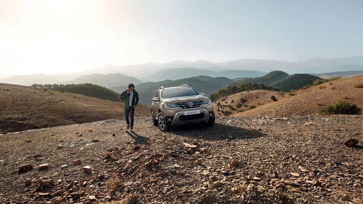 A man walking beside his parked All-New Renault Duster in a hilly area